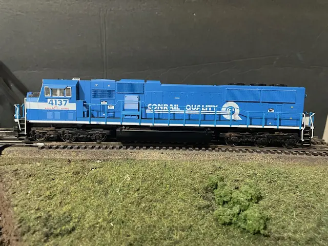 A blue train is on the tracks near some grass.